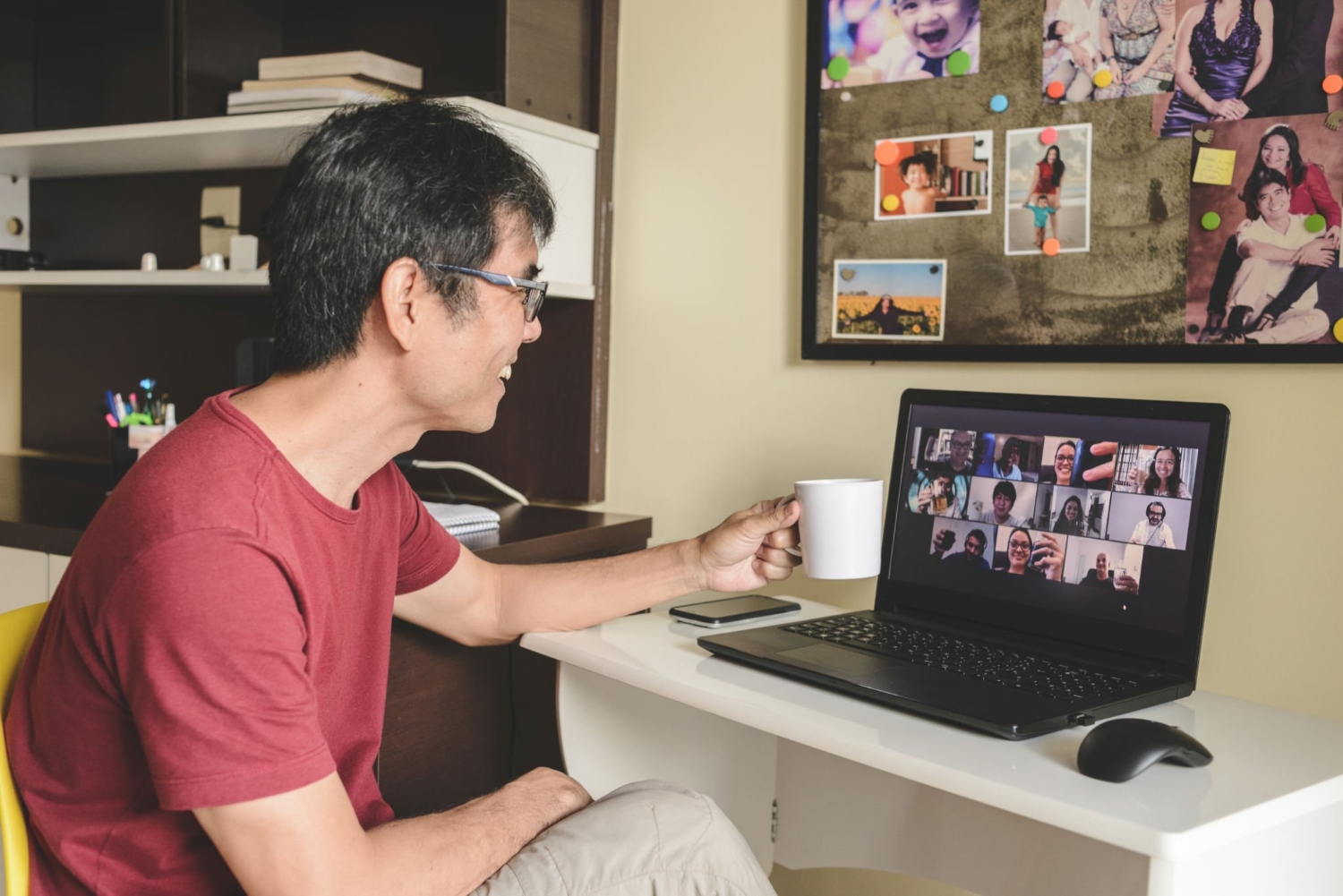 Man at home attending to a virtual happy hour with many people on screen toasting online together